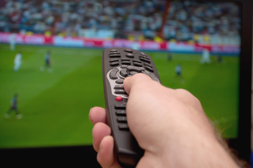 Afstandsbediening die naar een tv wijst waarop voetbal te zien is